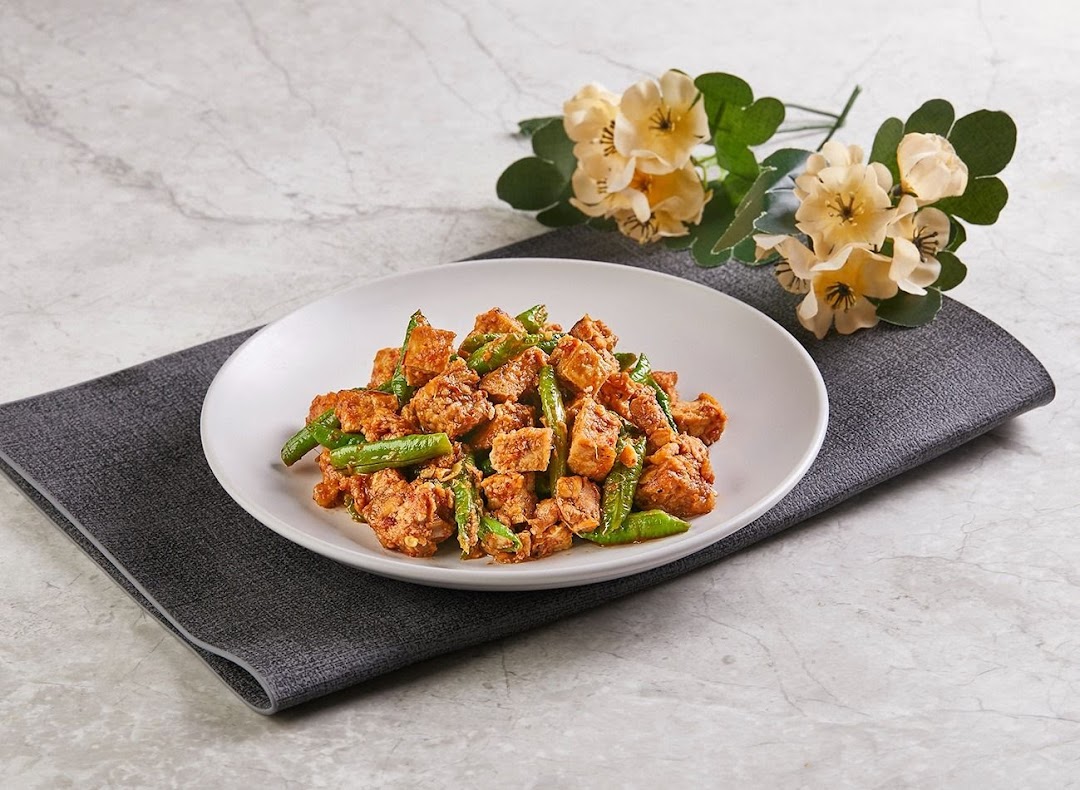 A vibrant dish of stir-fried tempeh and green beans on a white plate with floral decor.