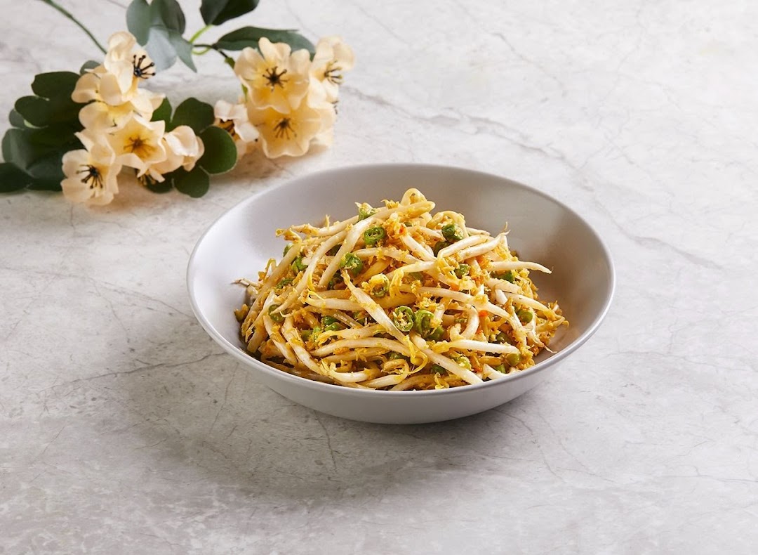 A bowl of stir-fried bean sprouts with green chilies and a yellow sauce, garnished with flowers.