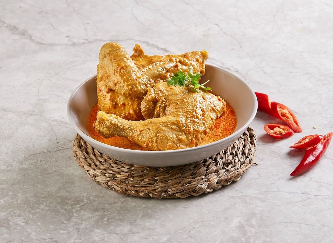 A bowl of chicken pieces in a rich, creamy orange sauce, garnished with cilantro and red chilies.