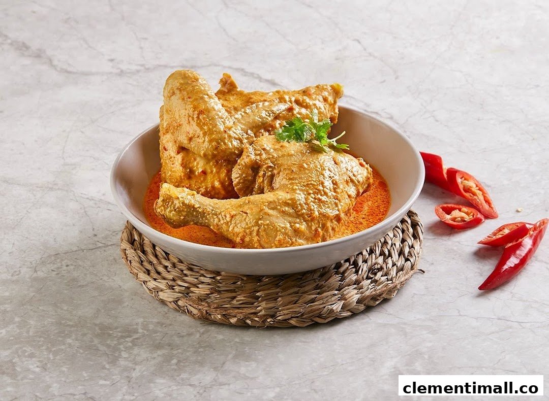 A bowl of chicken pieces in a rich, creamy orange sauce, garnished with cilantro and red chilies.