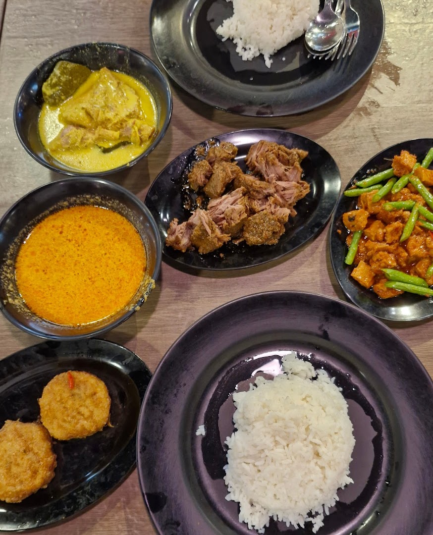 A vibrant spread of traditional Malay dishes, including rice, curries, and fried items, on a wooden table.