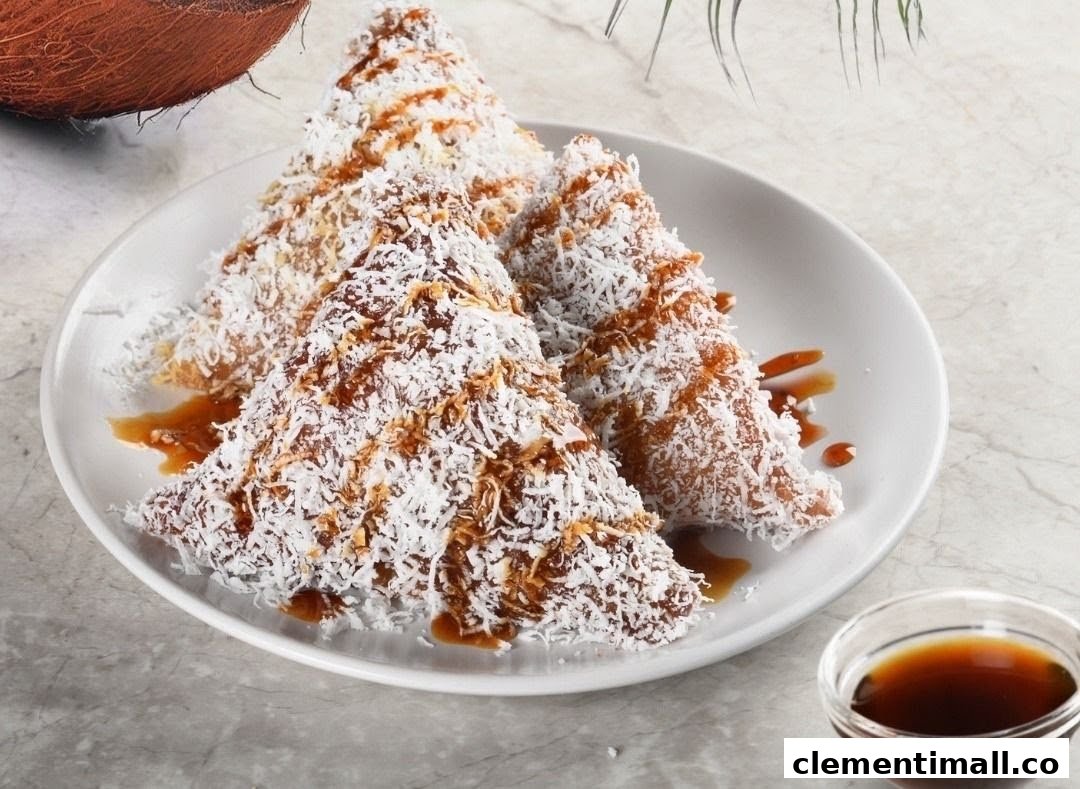 Three pyramid-shaped pastries covered in shredded coconut and drizzled with a sweet brown sauce, served on a white plate.