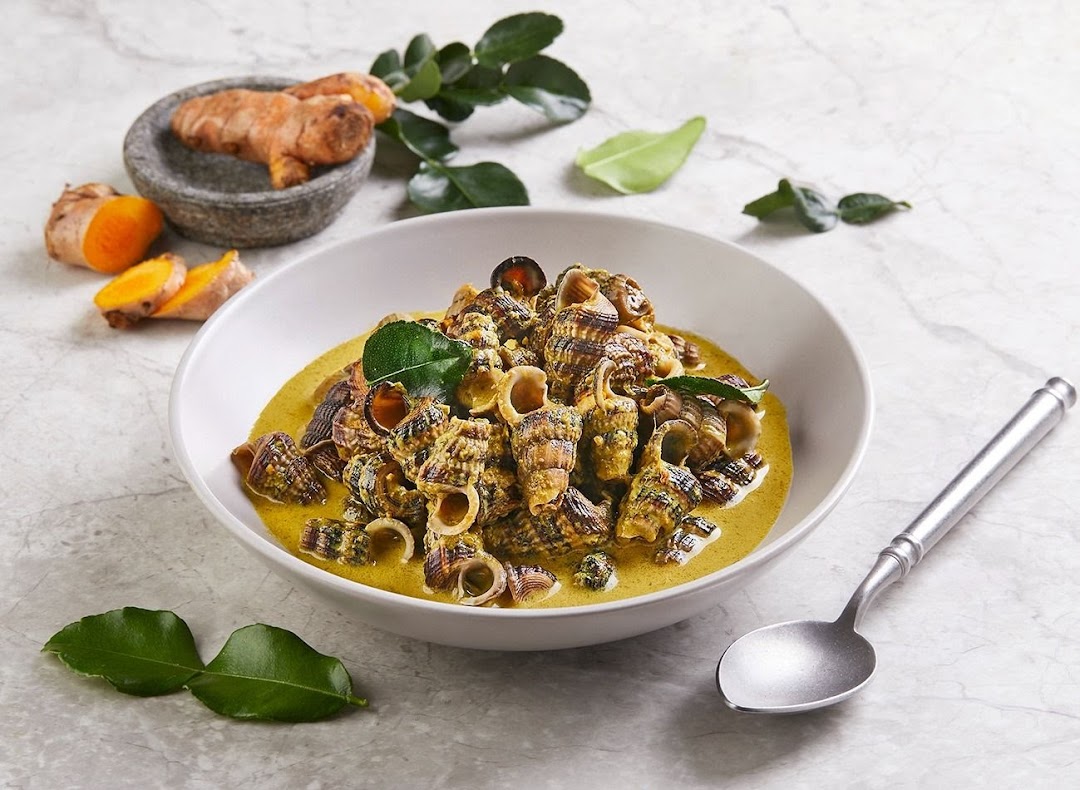 A bowl of sea snails (siput sedut) in a rich yellow coconut curry, garnished with kaffir lime leaves and turmeric.