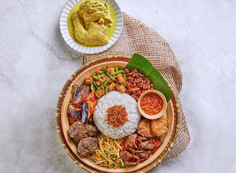 A vibrant platter of traditional Malay/Indonesian dishes including rice, vegetables, meats, and a side of chicken.