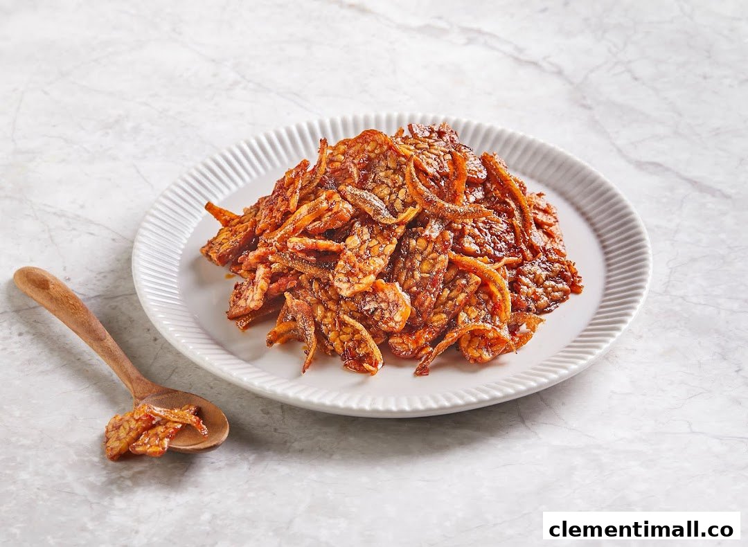A plate of crispy, glazed tempeh and anchovies with a wooden spoon on a light marble surface.