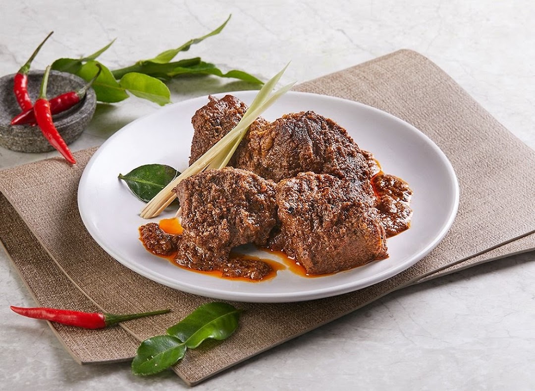 A plate of rich, saucy beef rendang garnished with lemongrass, kaffir lime leaves, and red chilies.