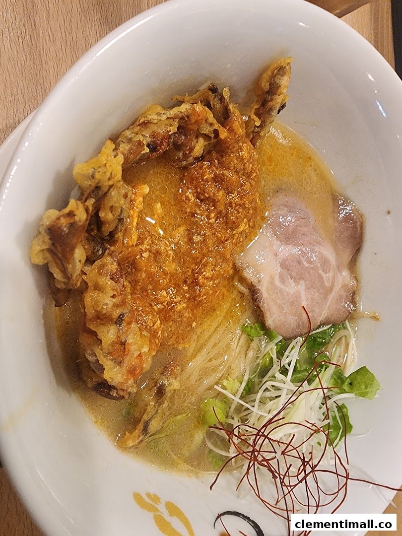 A close-up of a delicious ramen bowl featuring crispy soft-shell crab, chashu, and fresh garnishes.