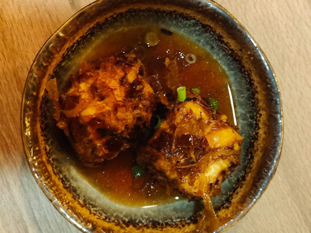 A close-up of two savory, deep-fried items in a rich brown sauce, garnished with green onions.