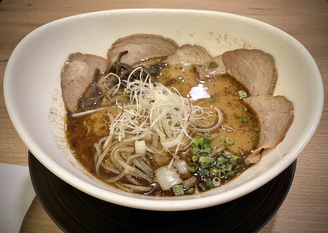 A close-up of a delicious bowl of ramen with pork slices, noodles, and various garnishes.