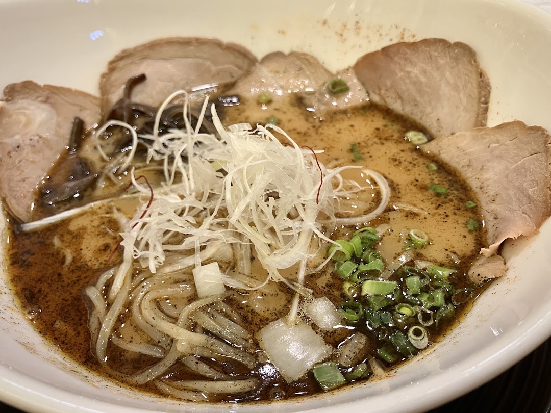 A close-up of a rich ramen bowl with sliced pork, noodles, and fresh garnishes.
