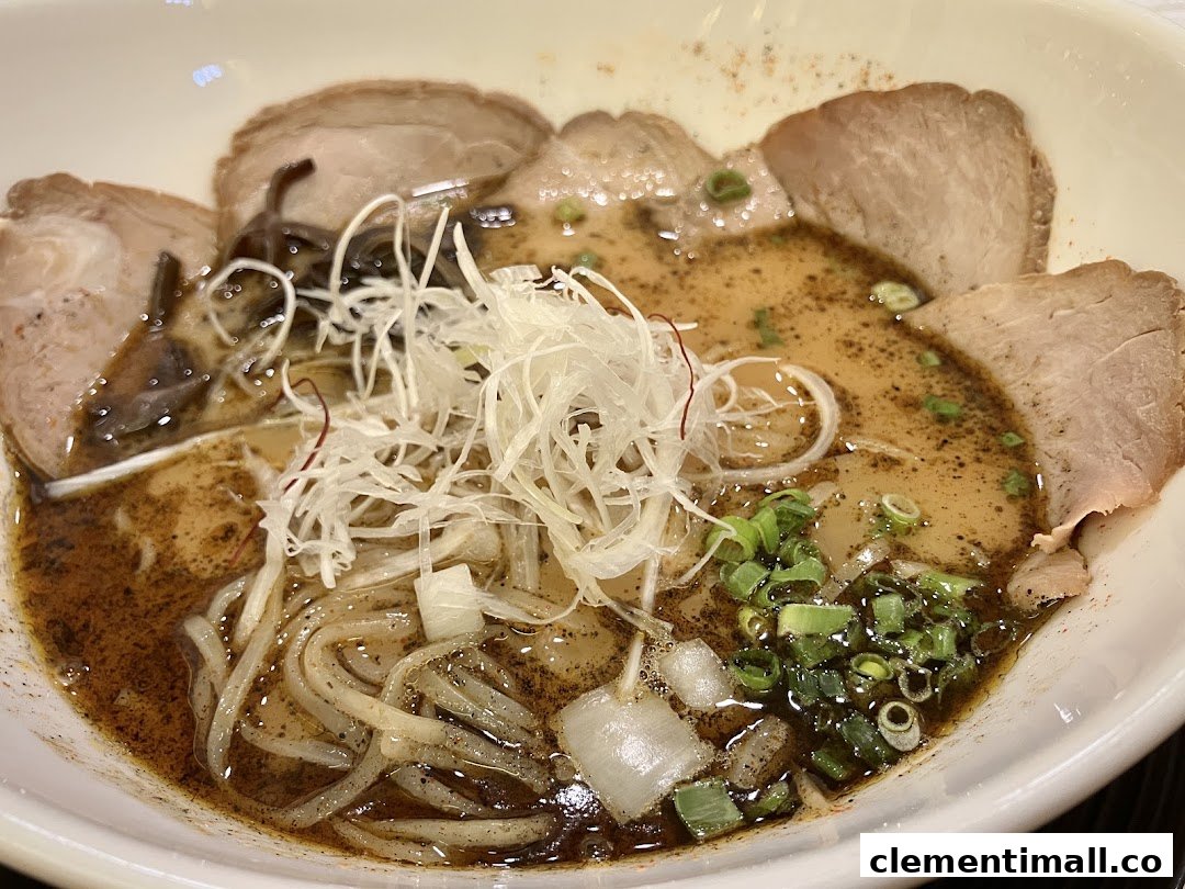 A close-up of a rich ramen bowl with sliced pork, noodles, and fresh garnishes.
