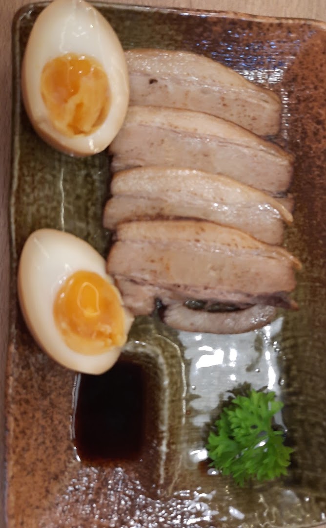 A close-up of a delicious side dish featuring tender pork belly slices and perfectly cooked soft-boiled eggs.