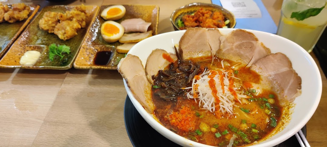 A vibrant bowl of ramen with chashu pork, accompanied by karaage, eggs, and a refreshing drink.
