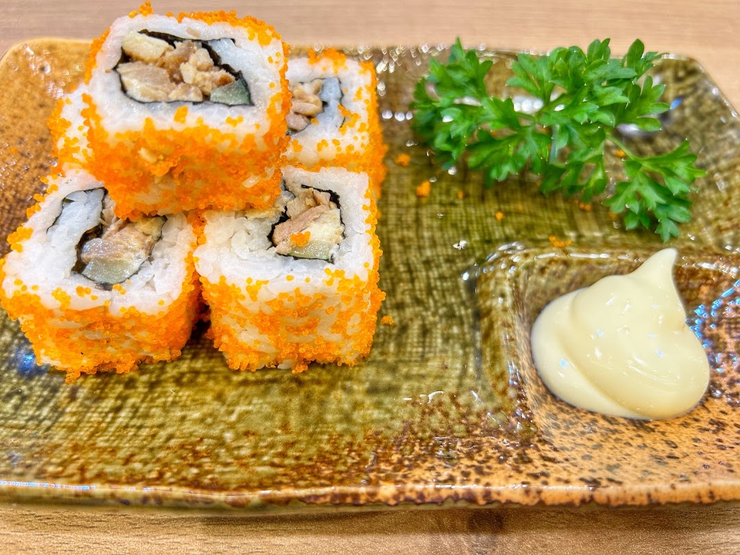 Close-up of vibrant sushi rolls with orange roe, served with mayonnaise and parsley on a rustic plate.