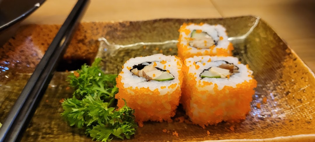 Three vibrant sushi rolls with orange roe and green garnish on a textured plate, with chopsticks.