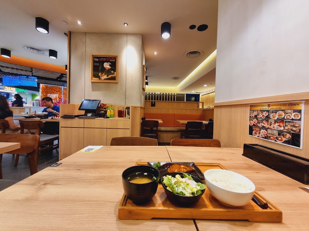A delicious meal set on a wooden table inside Hototogisu Ramen, with the restaurant interior and mall visible.