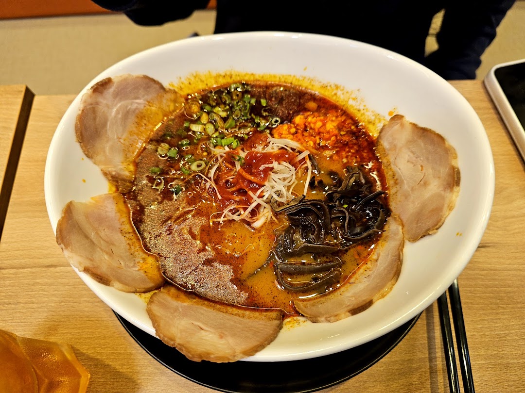A vibrant bowl of ramen with rich broth, sliced pork, and various toppings on a wooden table.