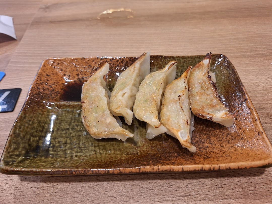 A plate of perfectly pan-fried gyoza with dipping sauce on a rustic ceramic dish.