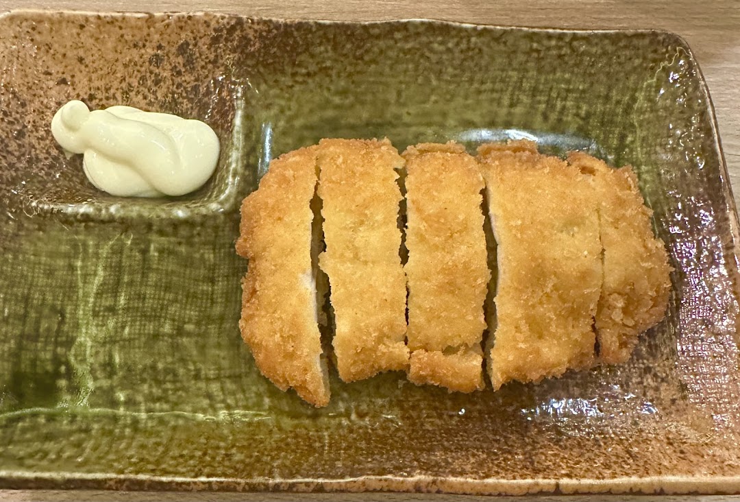 A golden-brown fried cutlet, sliced and served with a dollop of mayonnaise on a rustic plate.