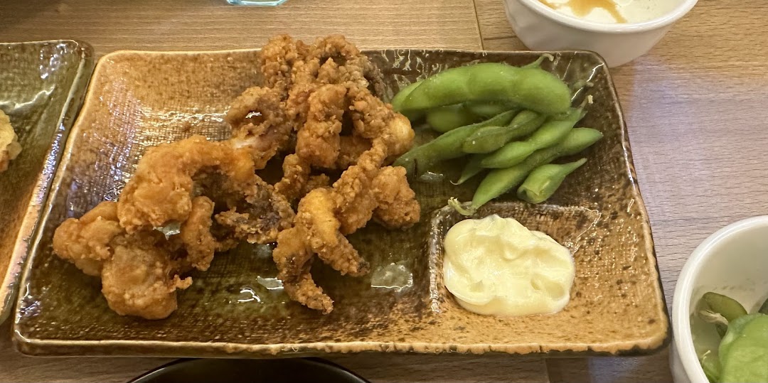 A plate of crispy fried calamari, fresh edamame, and creamy mayonnaise, served on a rustic dish.