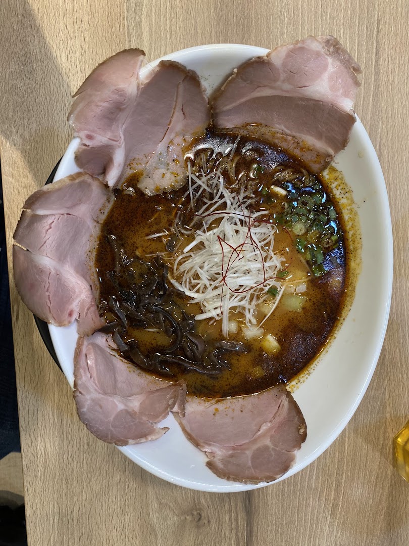 A close-up of a rich ramen bowl topped with tender chashu slices, shredded leeks, and wood ear mushrooms.