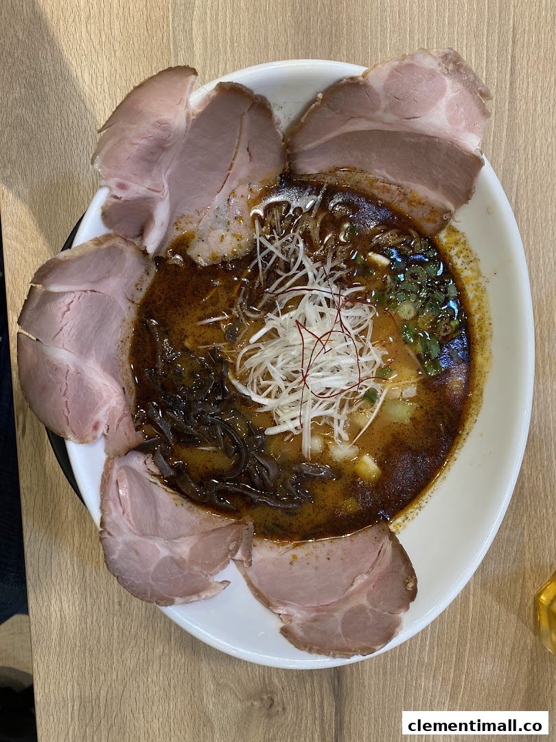 A close-up of a rich ramen bowl topped with tender chashu slices, shredded leeks, and wood ear mushrooms.