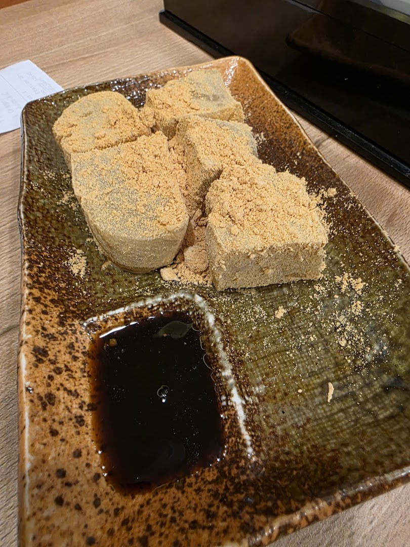 A plate of traditional Japanese warabi mochi dusted with kinako powder and served with kuromitsu syrup.