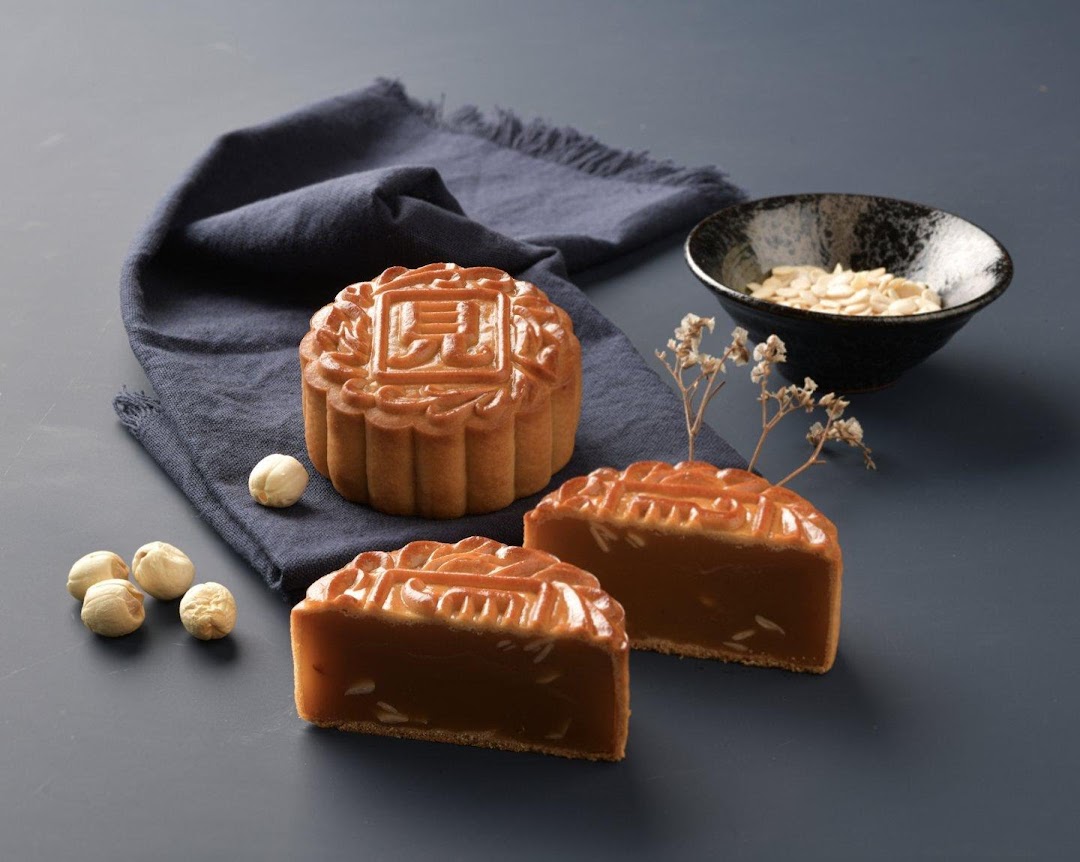 A whole and two sliced mooncakes with nuts and a bowl of almonds on a dark background.
