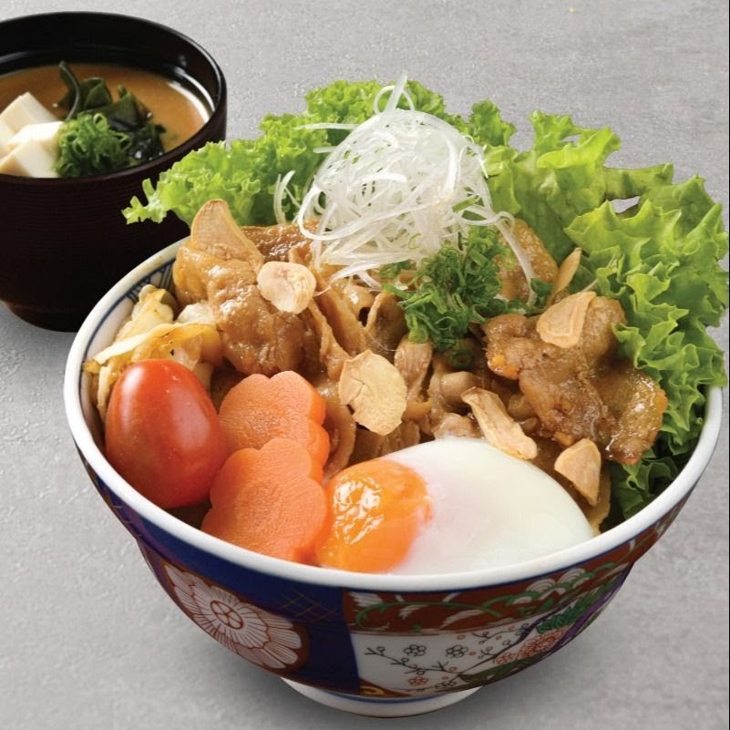A vibrant Japanese rice bowl featuring tender meat, fresh vegetables, a poached egg, and a side of miso soup.