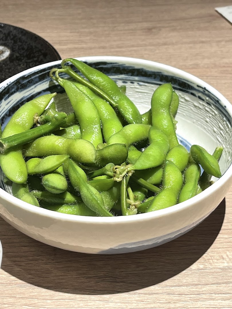A close-up of a bowl of vibrant green edamame pods on a wooden table.