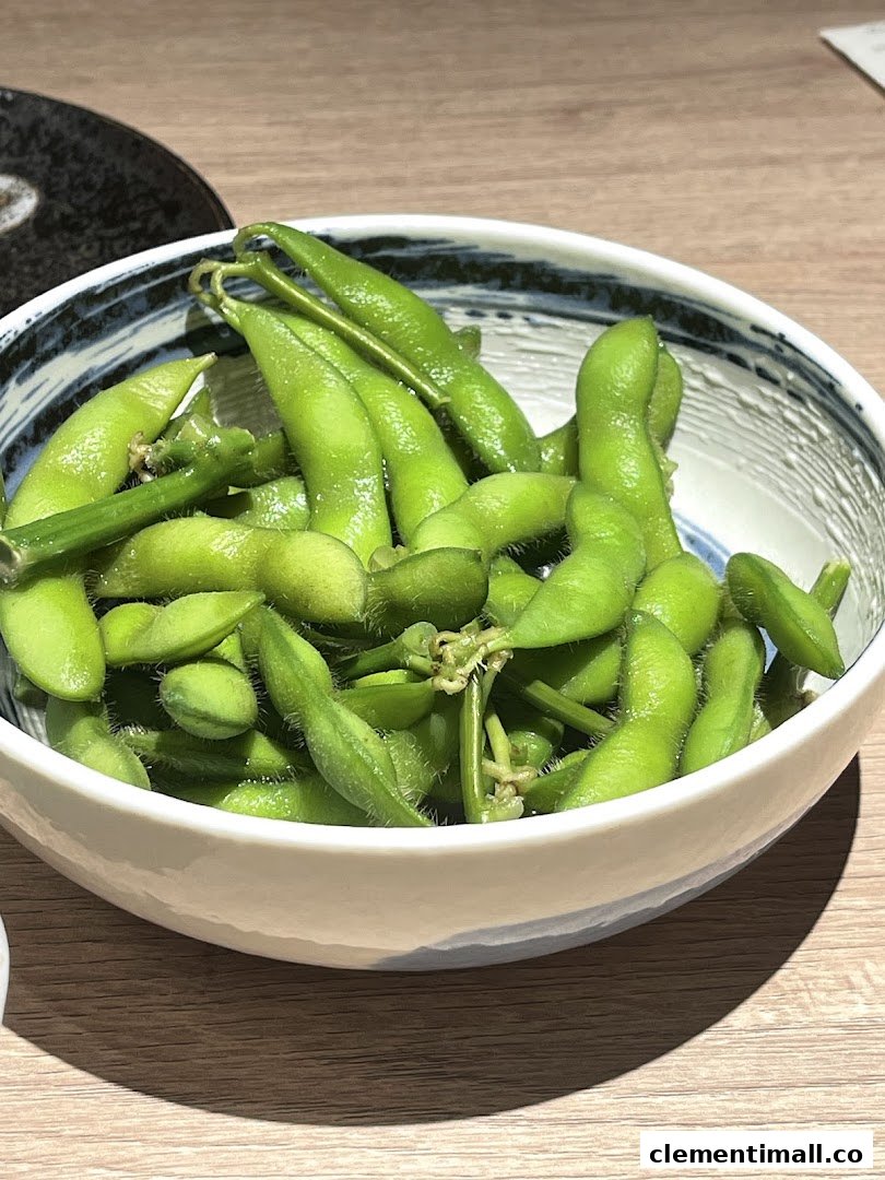 A close-up of a bowl of vibrant green edamame pods on a wooden table.