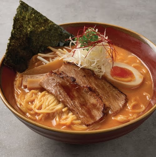 A vibrant bowl of ramen featuring chashu pork, a soft-boiled egg, seaweed, and fresh vegetables.