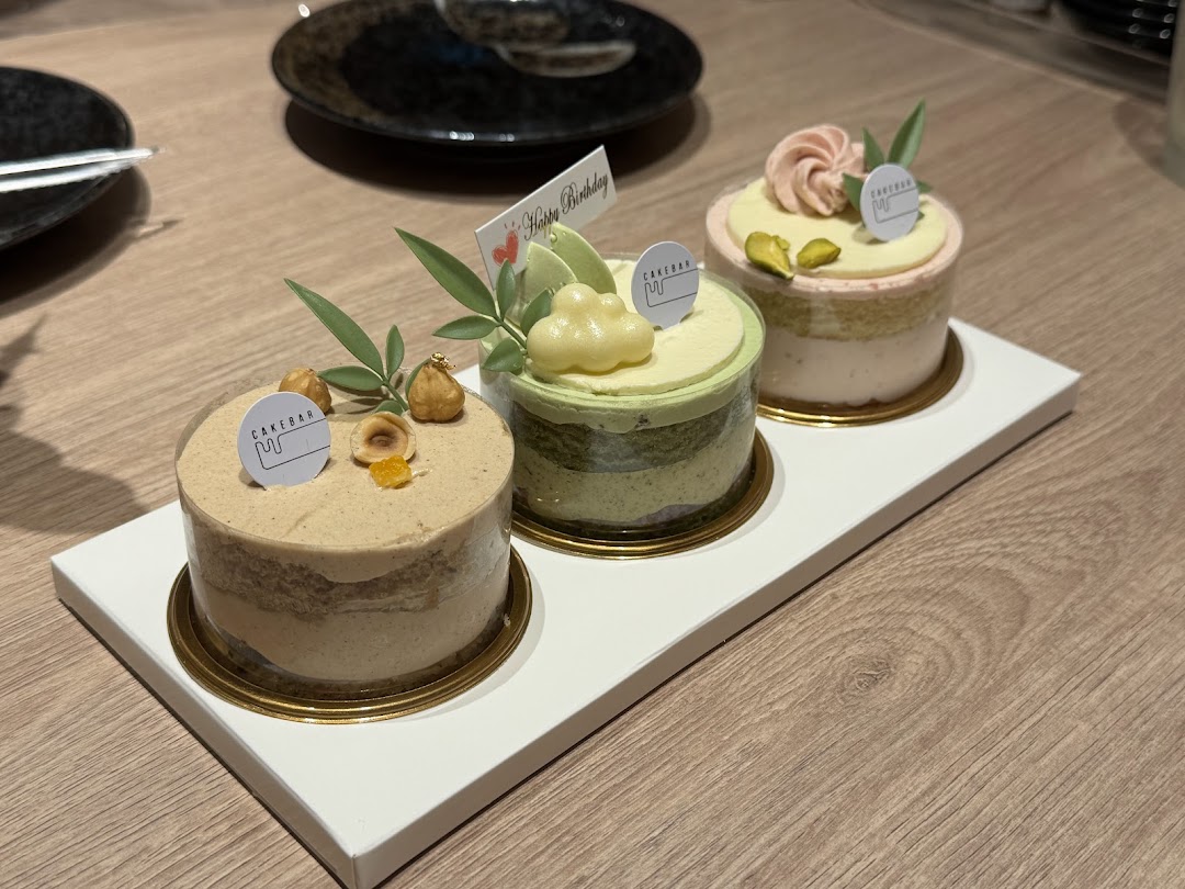 Three beautifully decorated individual cakes from Cakebar, served on a white tray at a dining table.