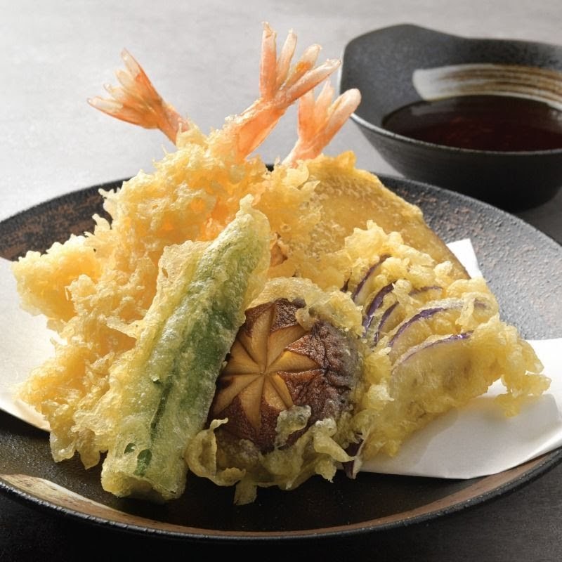 A plate of crispy golden tempura featuring shrimp, mushroom, and various vegetables with a dipping sauce.