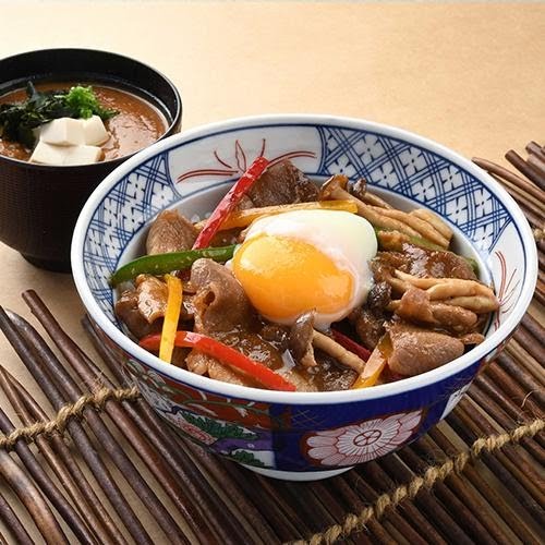 A Japanese donburi bowl featuring meat, mushrooms, vegetables, and a poached egg, served with a side of miso soup.