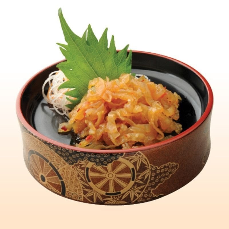 A close-up of a Japanese appetizer, possibly seasoned jellyfish, served in a decorative bowl with a green shiso leaf.