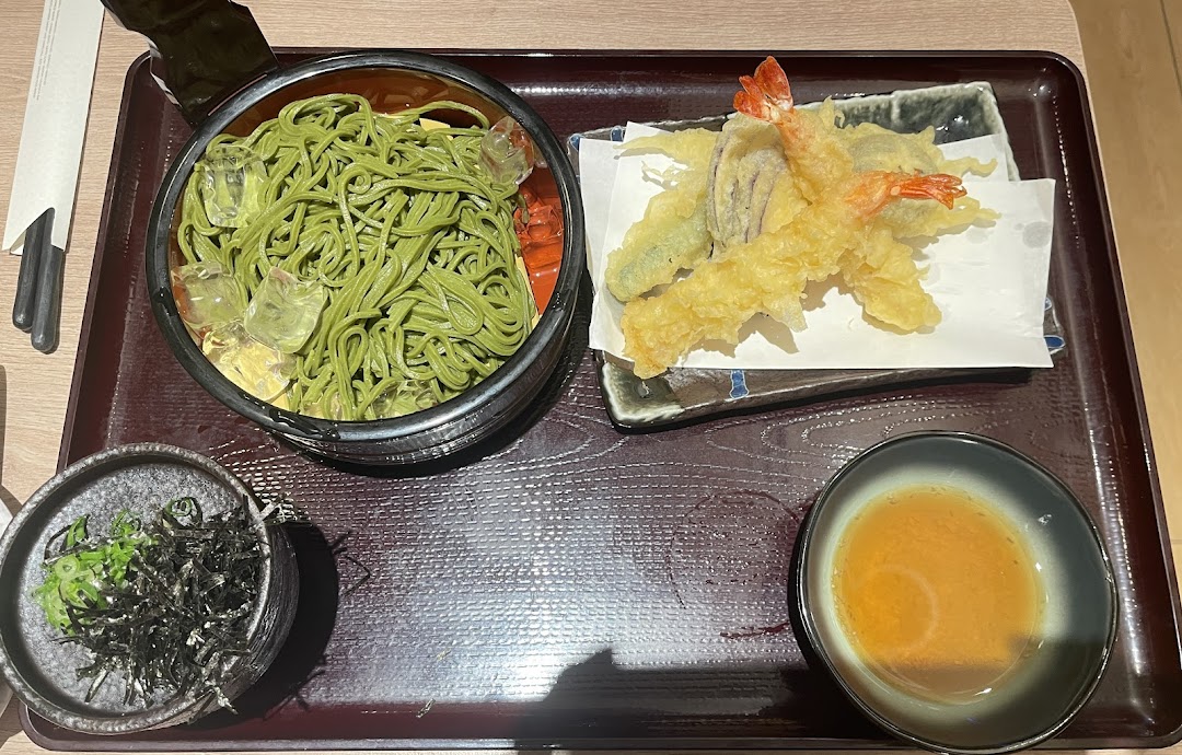 A delicious Japanese meal featuring green tea soba noodles with tempura and dipping sauce.