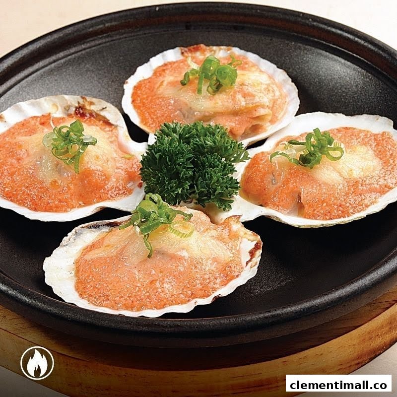 Four baked scallops in shells, topped with cheese and spring onions, served on a dark plate.