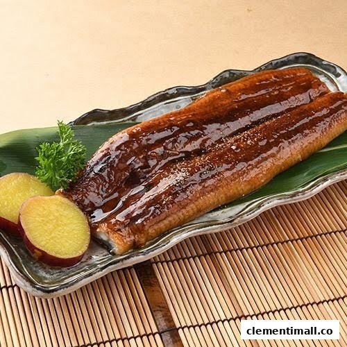 A glazed grilled eel (unagi) dish served on a leaf-lined plate with sweet potato slices.