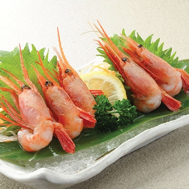 A plate of five cooked shrimp garnished with lemon, parsley, and shiso leaves.