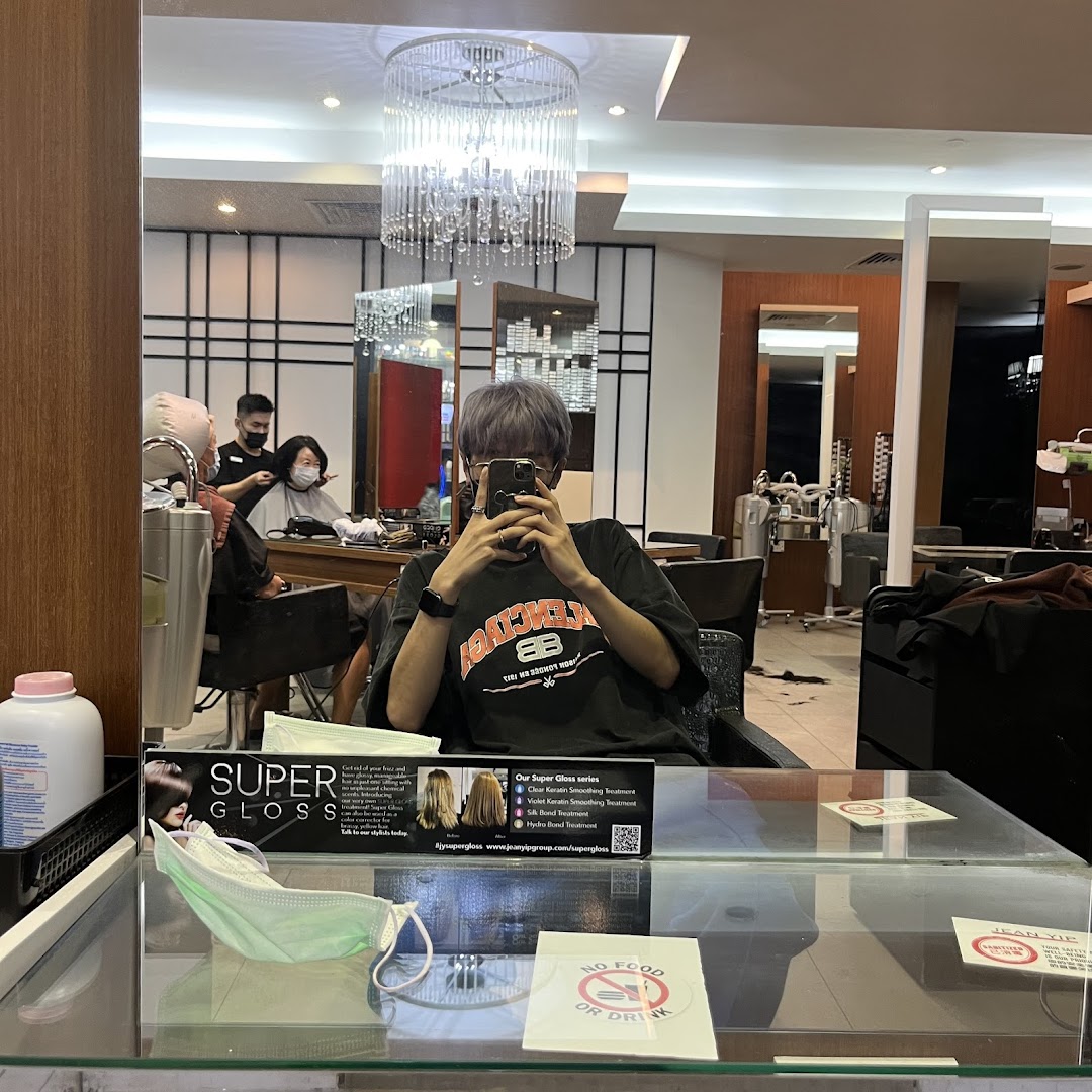A customer in a hair salon chair, reflected in a mirror, with staff attending to another client.