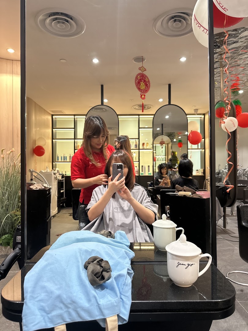 A customer receives a hair service from a stylist inside Jean Yip Hairdressing salon, reflected in a mirror.
