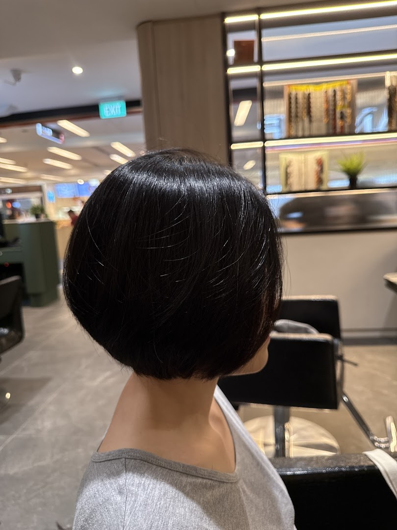 A person showcasing a freshly styled, sleek short bob haircut inside a hair salon.