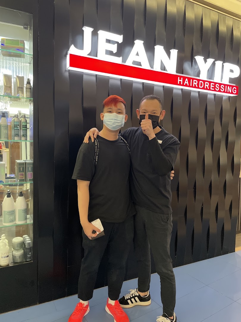 Two men, one giving a thumbs-up, stand proudly in front of the Jean Yip Hairdressing shop entrance.