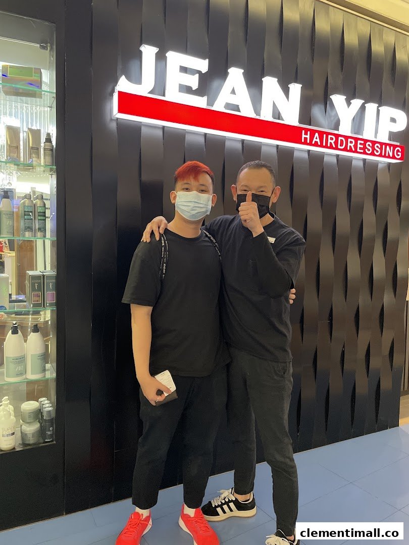 Two men, one giving a thumbs-up, stand proudly in front of the Jean Yip Hairdressing shop entrance.