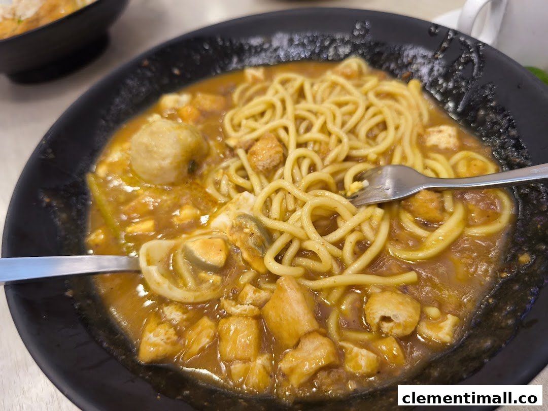 A close-up of a delicious noodle dish with a rich sauce, meatballs, and other ingredients in a black bowl.