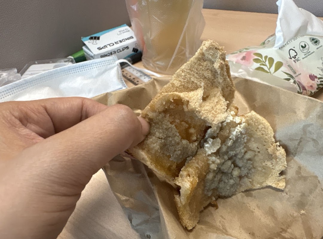 A hand holds a piece of sweet toast from Kaffe Toast Thai Noodle Bar, showing its delicious filling.