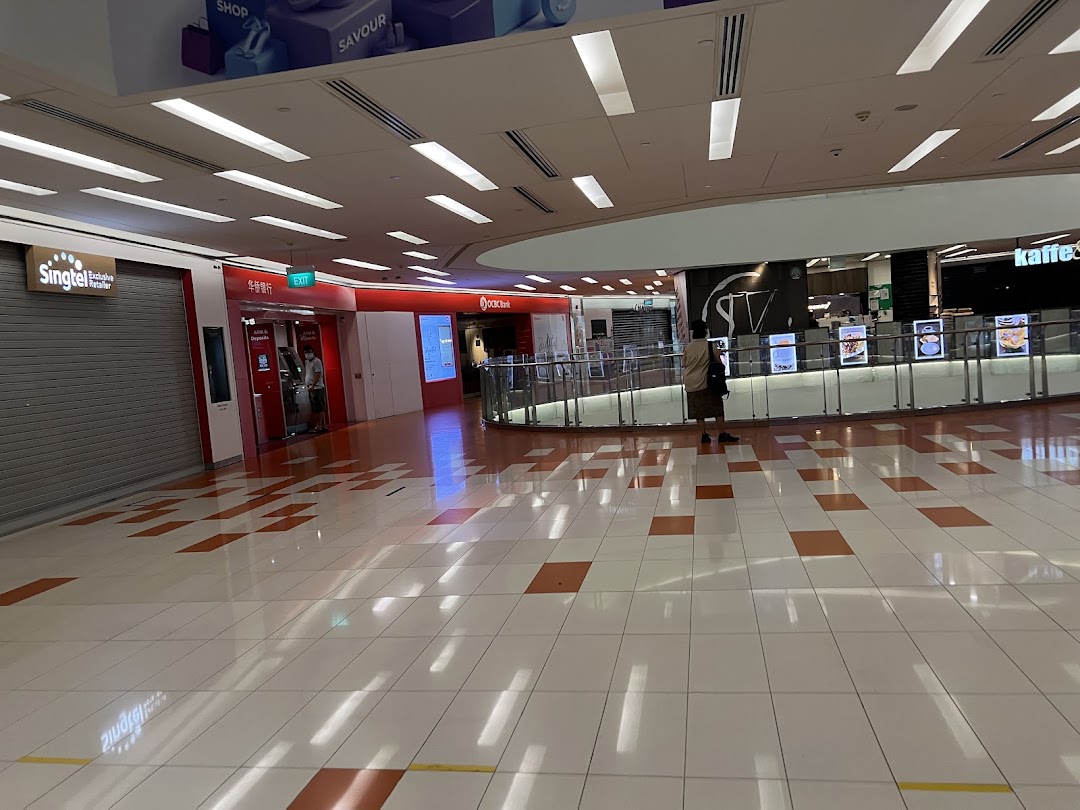 A wide shot of a brightly lit shopping mall interior with various shops and a person.