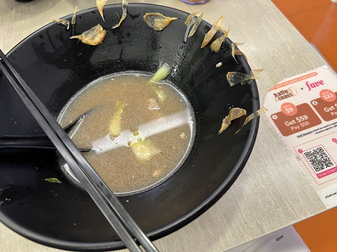 A half-eaten bowl of noodles with chopsticks and a promotional card from Kaffe Toast.