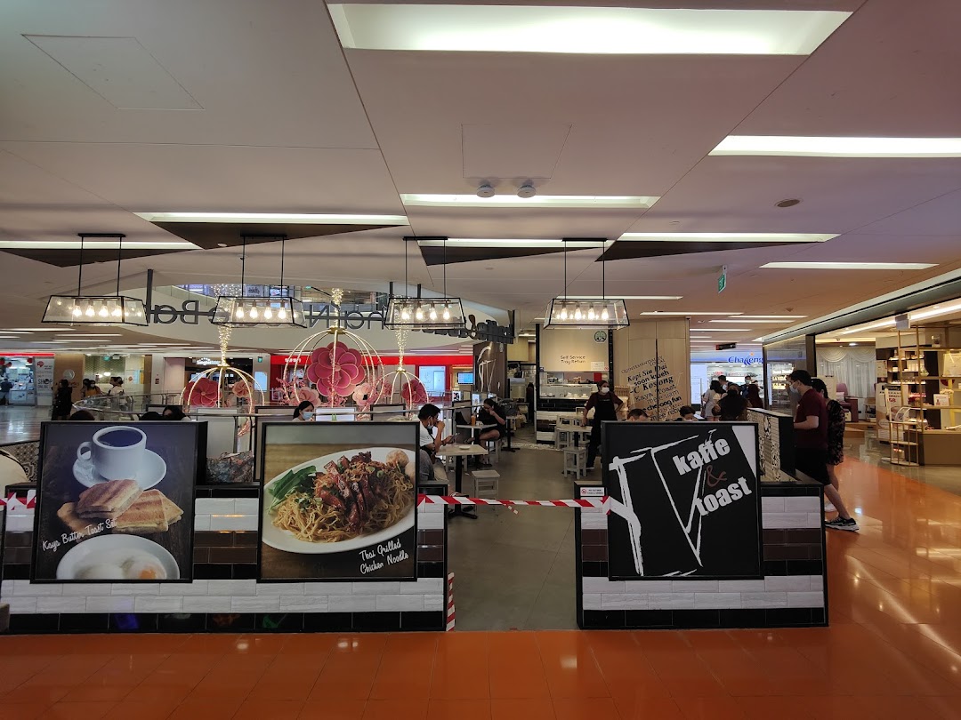 An interior view of Kaffe Toast Thai Noodle Bar, showcasing diners and promotional food displays.